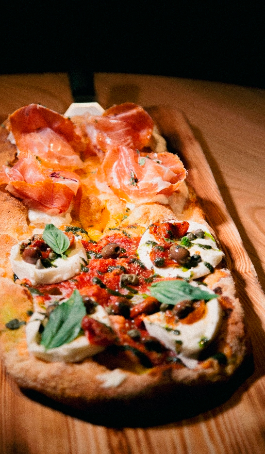 Una masa pala servida con tomate, queso, jamón, aceitunas y alcaparras.