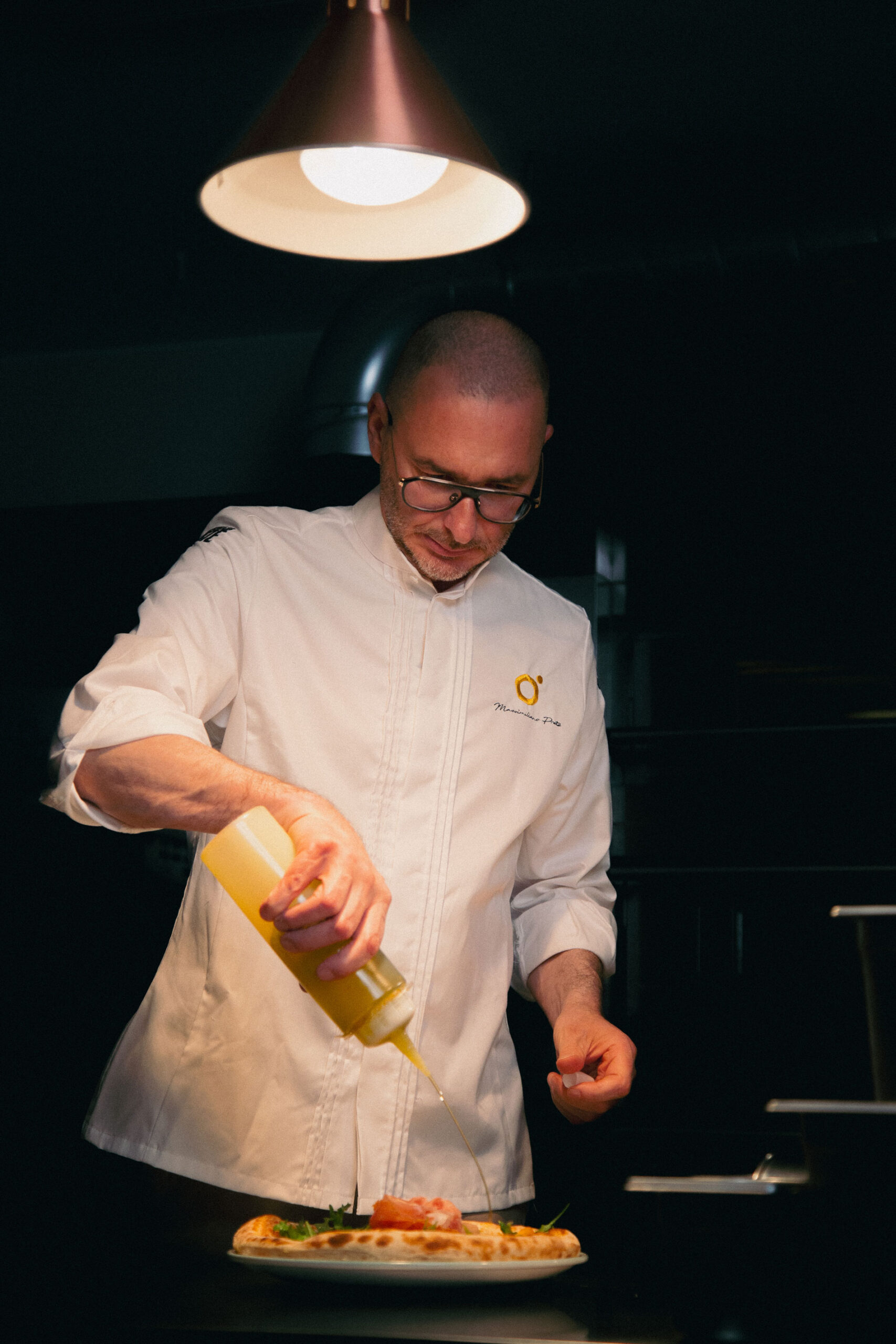 El chef Massimiliano Prete decorando una pizza con aceite en su cocina profesional